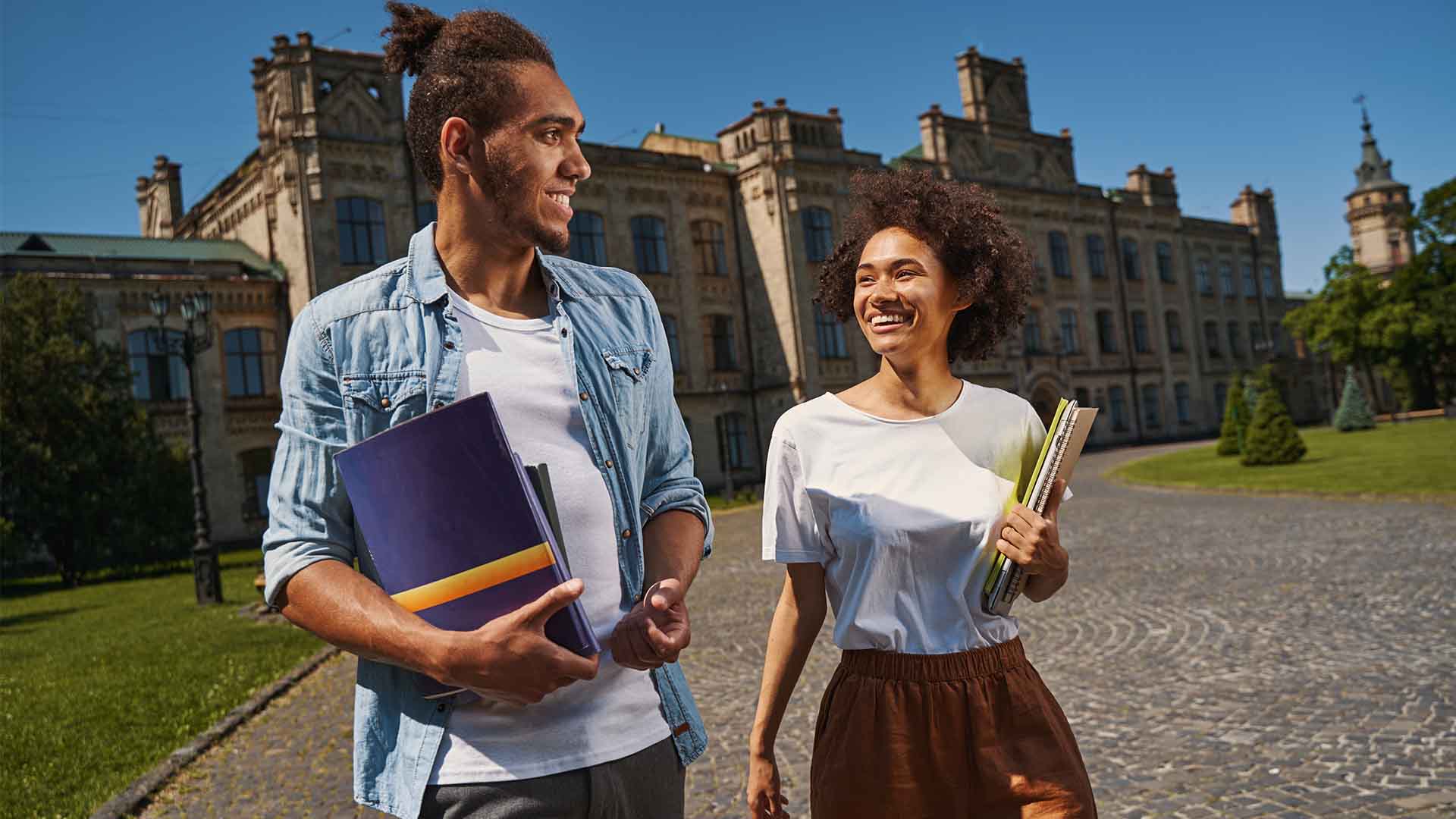 Two international students walking on a university campus in Germany, holding books and smiling — representing the German University Application Process