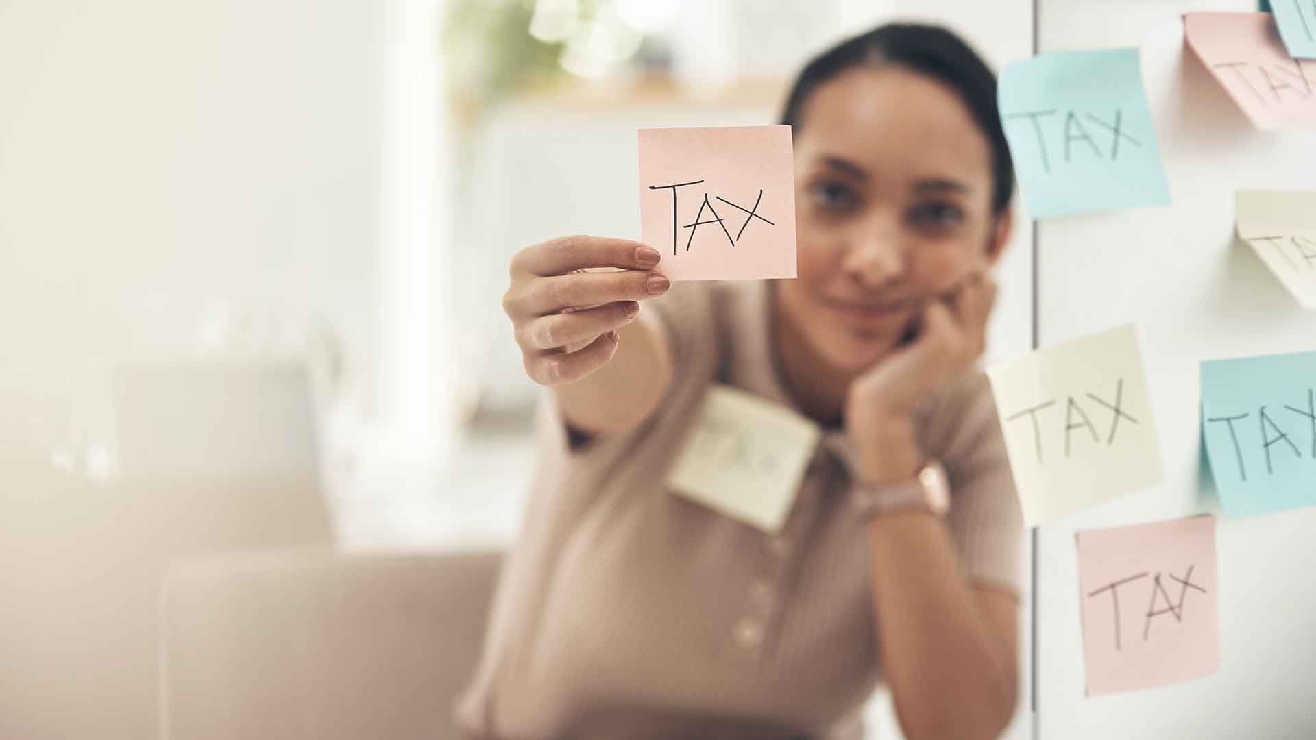 female expat holding a sticker with the word TAX — symbolizing How to Change Tax Class in Germany
