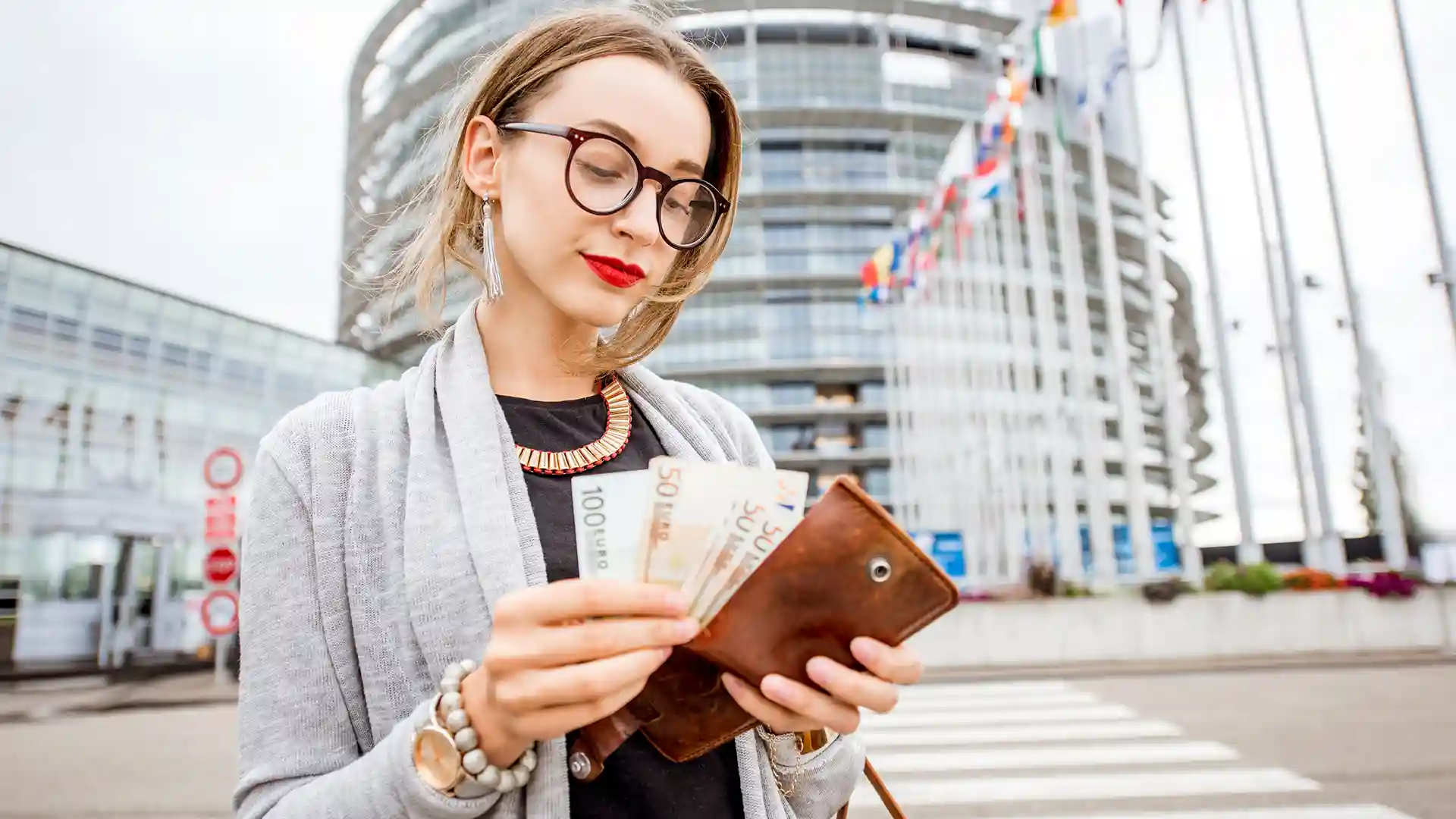 Young professional woman holding euro banknotes in front of a modern office building, representing average salary in Germany