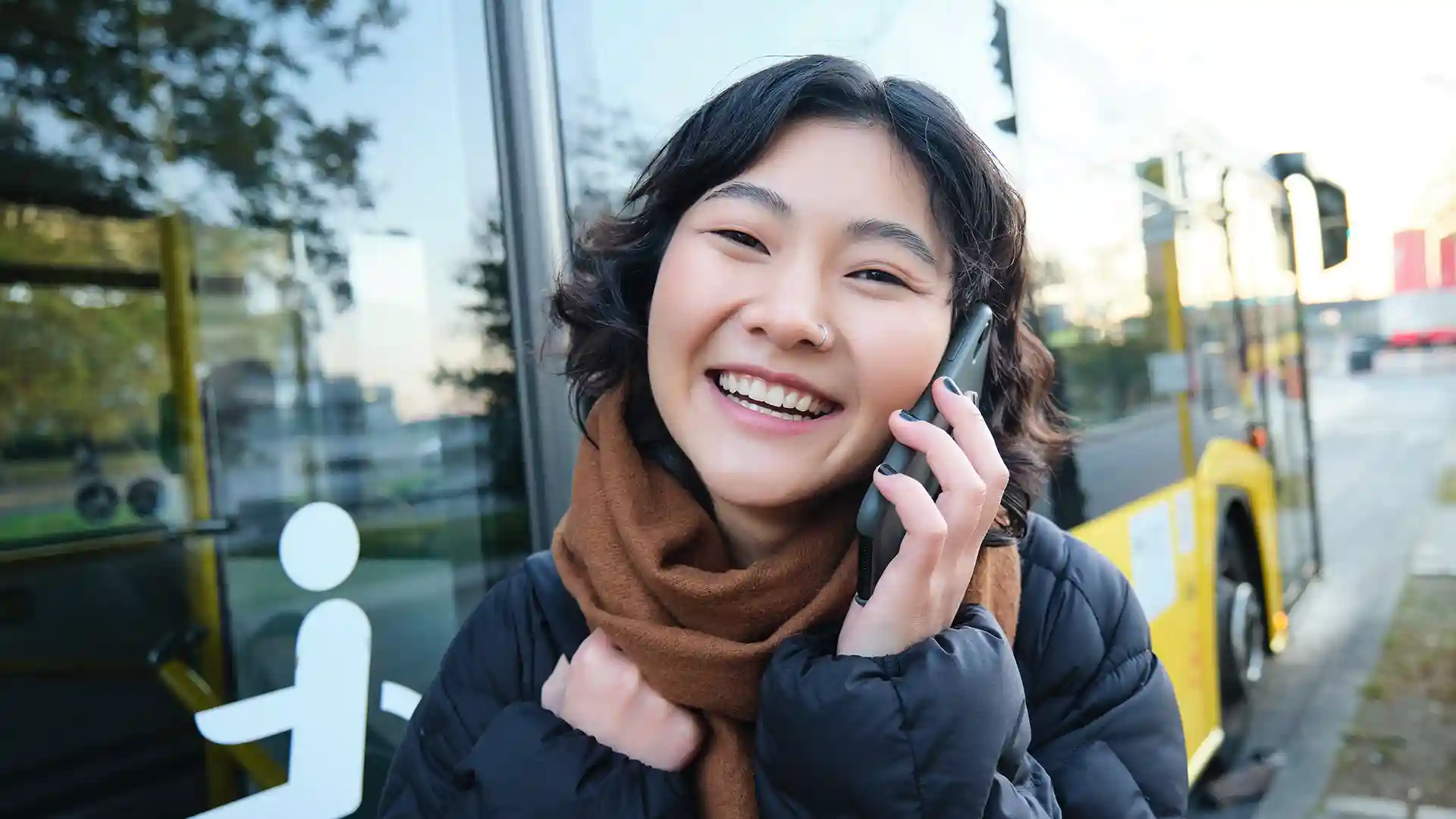 Happy young Asian woman in Berlin using smartphone to make a call, representing how to use and understand phone numbers in Germany.