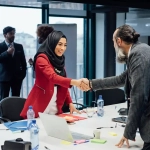 Businesswoman in a hijab shaking hands with a colleague during a job interview in a modern office — representing how to get a job in Germany without speaking German.