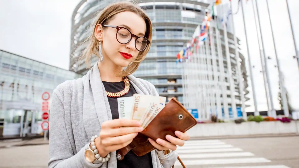 Young professional woman holding euro banknotes in front of a modern office building, representing average salary in Germany