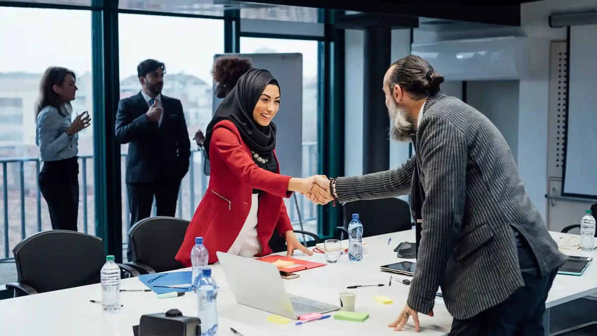 Businesswoman in a hijab shaking hands with a colleague during a job interview in a modern office — representing how to get a job in Germany without speaking German.