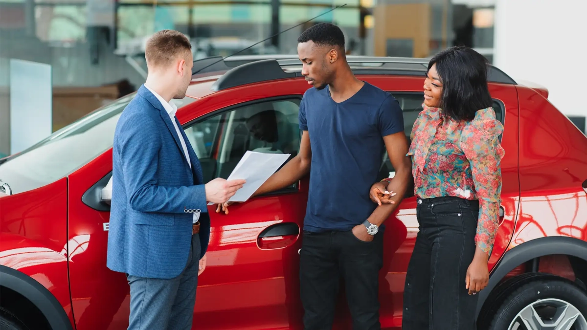 African American couple buying a car in Germany at a dealership while a salesperson shows them the vehicle.