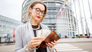 Young professional woman holding euro banknotes in front of a modern office building, representing average salary in Germany