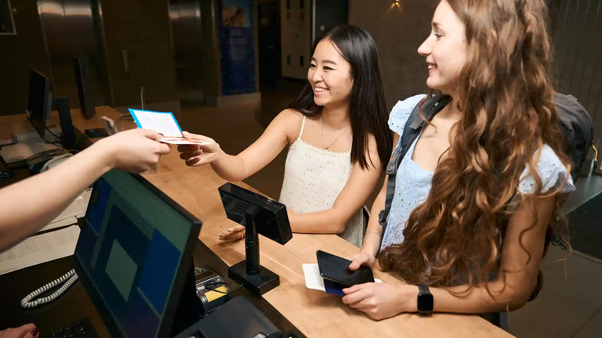 Two young female students opening a German bank account as student at a bank branch, discussing documents with a friendly bank advisor.